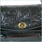 black leather bag with top flap closure and elaborate, tooled floral decoration